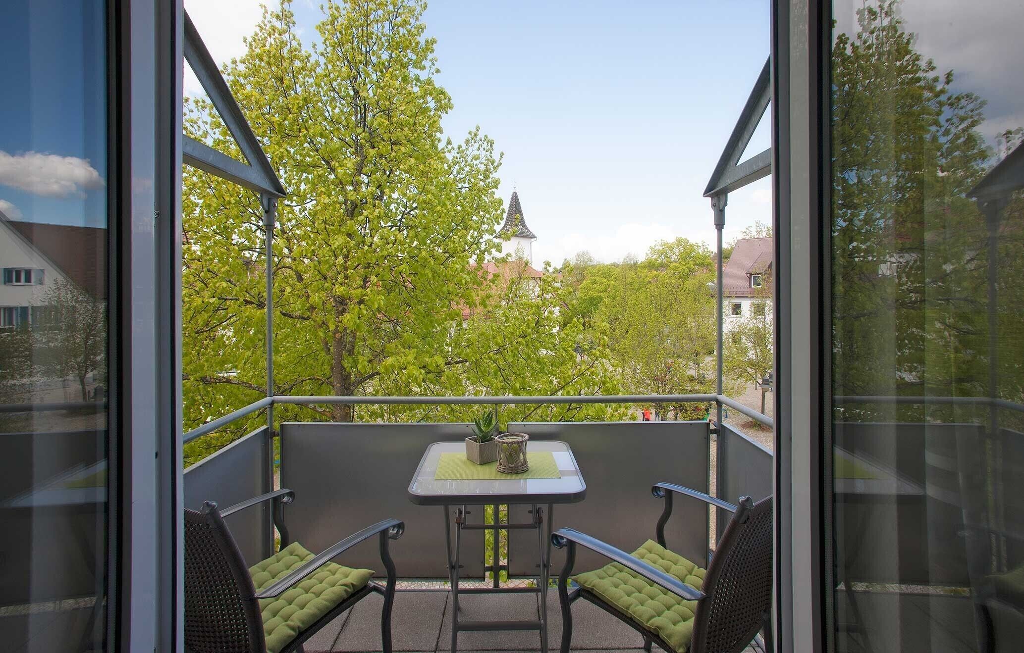 A balcony with a table, two chairs, and a view of trees and buildings.