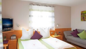 A hotel room with a bed, a sofa, a TV, a bedside table, and a window with curtains.
