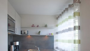 A modern kitchen with a built-in oven, coffee maker, and a sink. There are cabinets, a countertop, and a window with curtains.