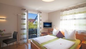 A hotel room with a balcony, a television, a desk, and a bed with pillows.
