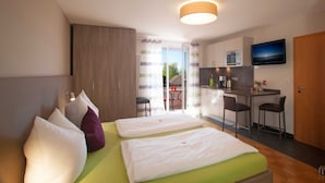 Ein Hotelzimmer mit zwei Betten, einer Küchenzeile, einem Fernseher und einer Schiebetür zu einem Außenbereich.