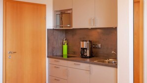 Una cucina compatta con forno a microonde, macchina del caffè e un portauovili verde.