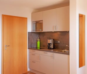 Una cocina compacta con microondas, cafetera y un portalapices verde.
