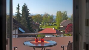 Un balcone con una porta in vetro, un tavolo rotondo con sedie e vista su un quartiere residenziale con case e alberi.