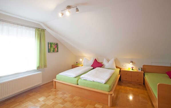 Ein Zimmer mit schrägen Wänden, einem Bett mit grüner Bettwäsche, einem Nachttisch mit Lampe und einem Heizkörper.