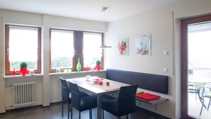 Ein Essbereich mit Tisch, Stühlen, einer Bank und Fenstern mit Blumentöpfen.