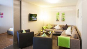 Ein modernes Wohnzimmer mit einer Couch, zwei Sesseln, einem Couchtisch und einem an der Wand befestigten Flachbildfernseher.