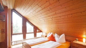 A bedroom with a wooden ceiling, a bed with white and orange bedding, a nightstand with a lamp, and a window with a view of trees. - Apartment '2' with Balcony and Wi-Fi (Wasserburg (Bodensee))