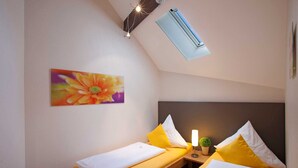 Ein kleines Hotelzimmer mit zwei Betten, einem Deckenventilator, einer Klimaanlage und einem Blumengemälde an der Wand.