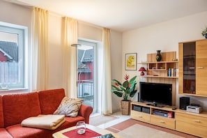 A living room with a red sofa, a television, wooden shelves, and a potted plant.