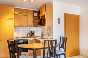 A kitchen with wooden cabinets, a stove, a sink, and two chairs.