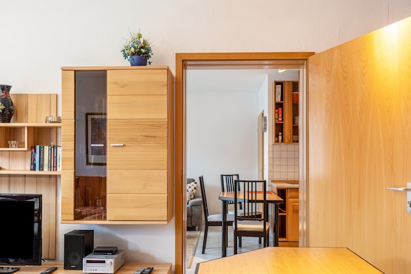 A compact living space with a wooden cabinet, a television, a small table, and a dining area.