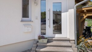 Fachada blanca con puerta, escalones, buzón y jardinera con flores.