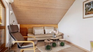 Una sala de estar acogedora con techo de madera, un sofá, un sillón reclinable y una mesa de centro con adornos.