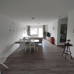 A modern kitchen with a dining area, wooden flooring, and a large wall clock.