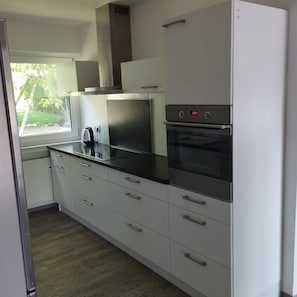 Eine moderne Küche mit Edelstahlgeräten, weißen Schränken und einem Fenster mit Blick auf Grünflächen.