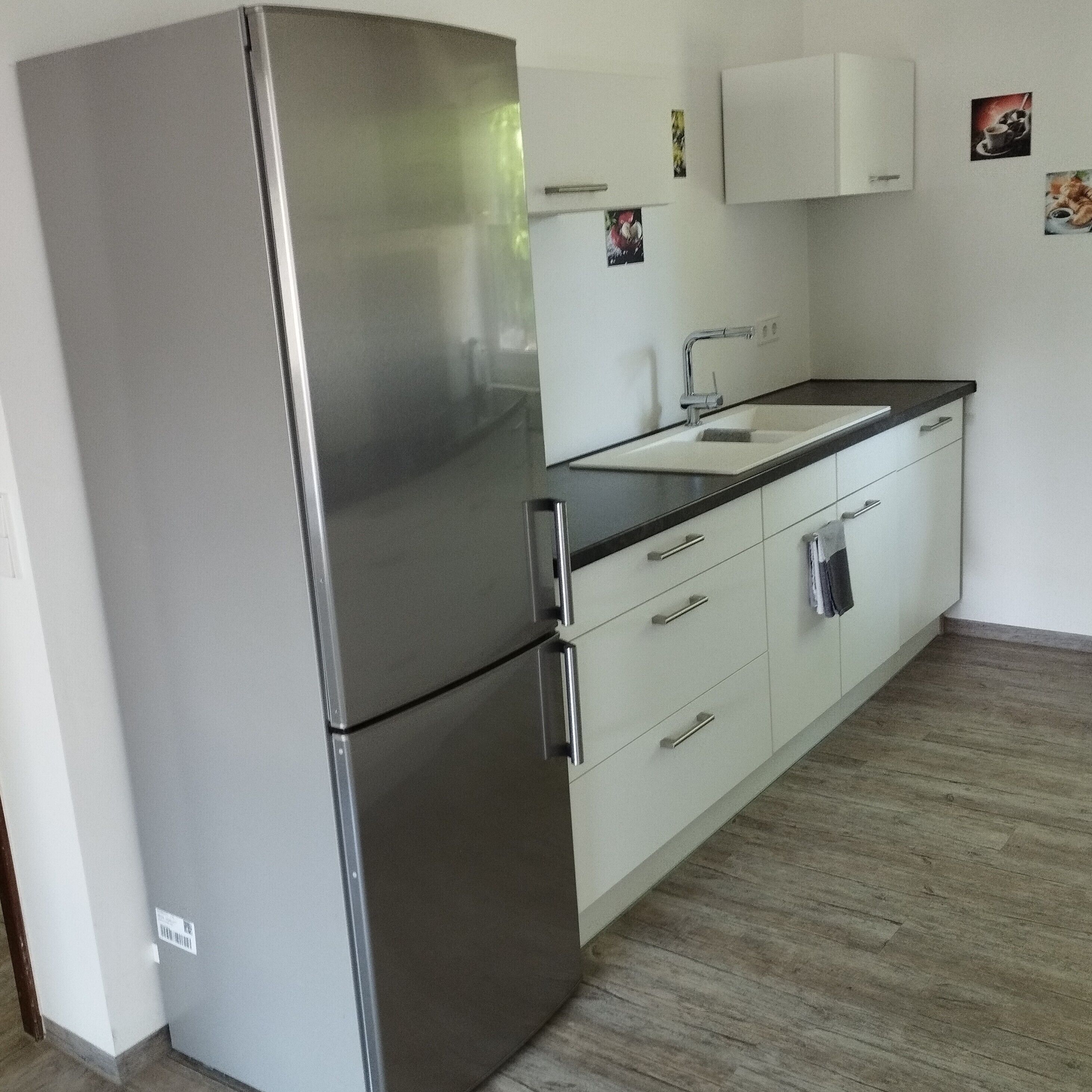 A kitchen with a stainless steel refrigerator, a sink, and white cabinets.