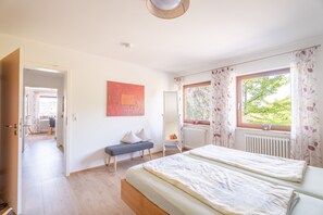 Une chambre avec deux lits, un banc, un radiateur et une fenêtre avec des rideaux.