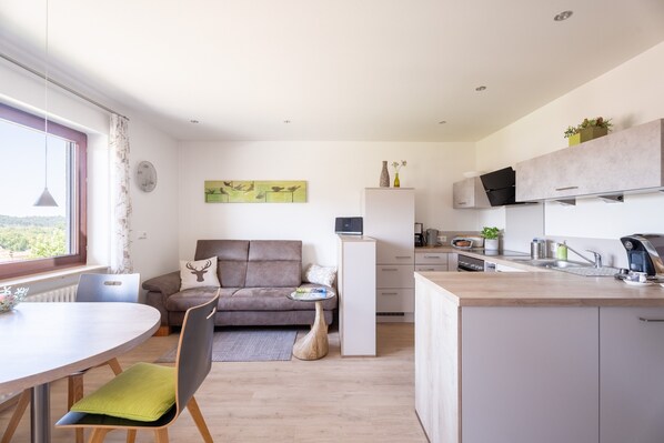 Un espace de vie moderne comprenant un coin repas, un canapé, une cuisine et une vue sur l’extérieur.