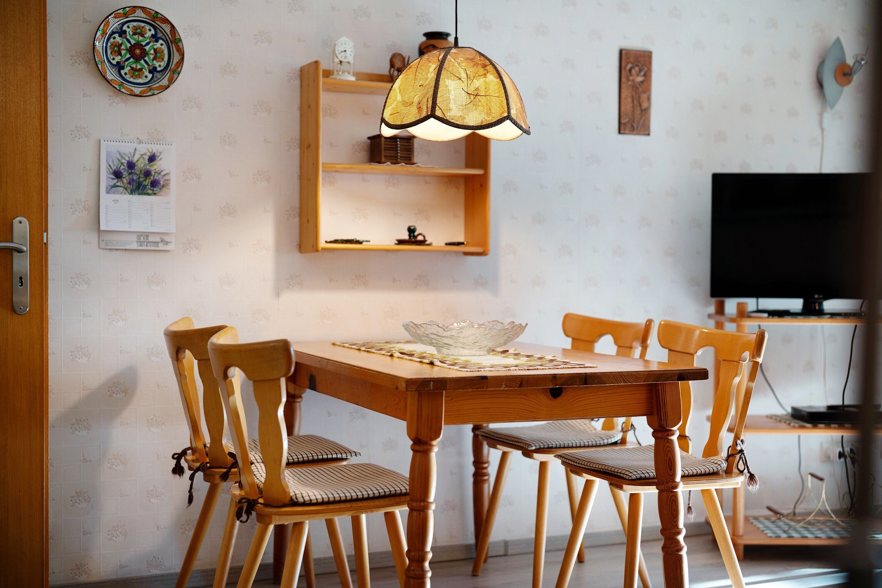 Un comedor con una mesa de madera, sillas, una lámpara colgante y un televisor al fondo.
