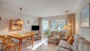 Una sala de estar con una mesa de comedor de madera, sillas, un sofá y una televisión.