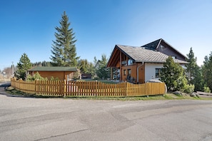 A two-story wooden cabin with a fenced yard, surrounded by trees.