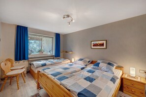 Un dormitorio con dos camas, una ventana con cortinas, una silla, una mesita de noche con lámpara y un cuadro en la pared.