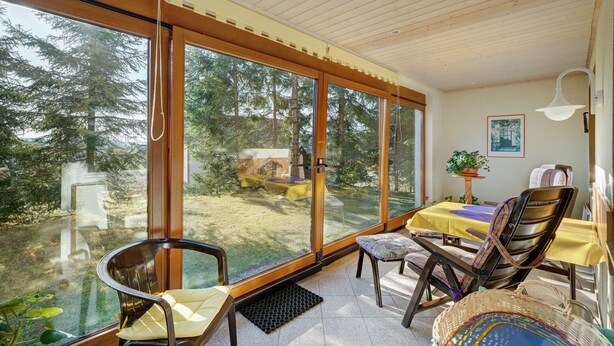 Una habitación con grandes puertas correderas de vidrio, una mesa de comedor con mantel amarillo y una silla con asiento tejido.