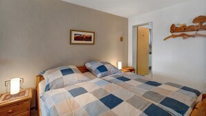 Un dormitorio con cama, mesita de noche, lámpara de noche, un cuadro enmarcado en la pared y un perchero de madera.