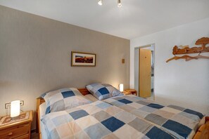 Une chambre à coucher comprenant un lit, une table de chevet, une lampe de chevet, un tableau encadré au mur et un porte-manteau en bois.