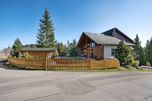 A two-story lodge with a wooden exterior, a fenced yard, and a clear sky.