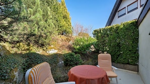 An outdoor seating area with two striped chairs and a table, surrounded by greenery and a building. - Studio '3' with Private Terrace, Shared Garden and Wi-Fi (Schönwald im Schwarzwald)