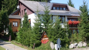 A two-story wooden house with a sloped roof, surrounded by evergreen trees and a sign indicating a hotel. - Studio '3' with Private Terrace, Shared Garden and Wi-Fi (Schönwald im Schwarzwald)