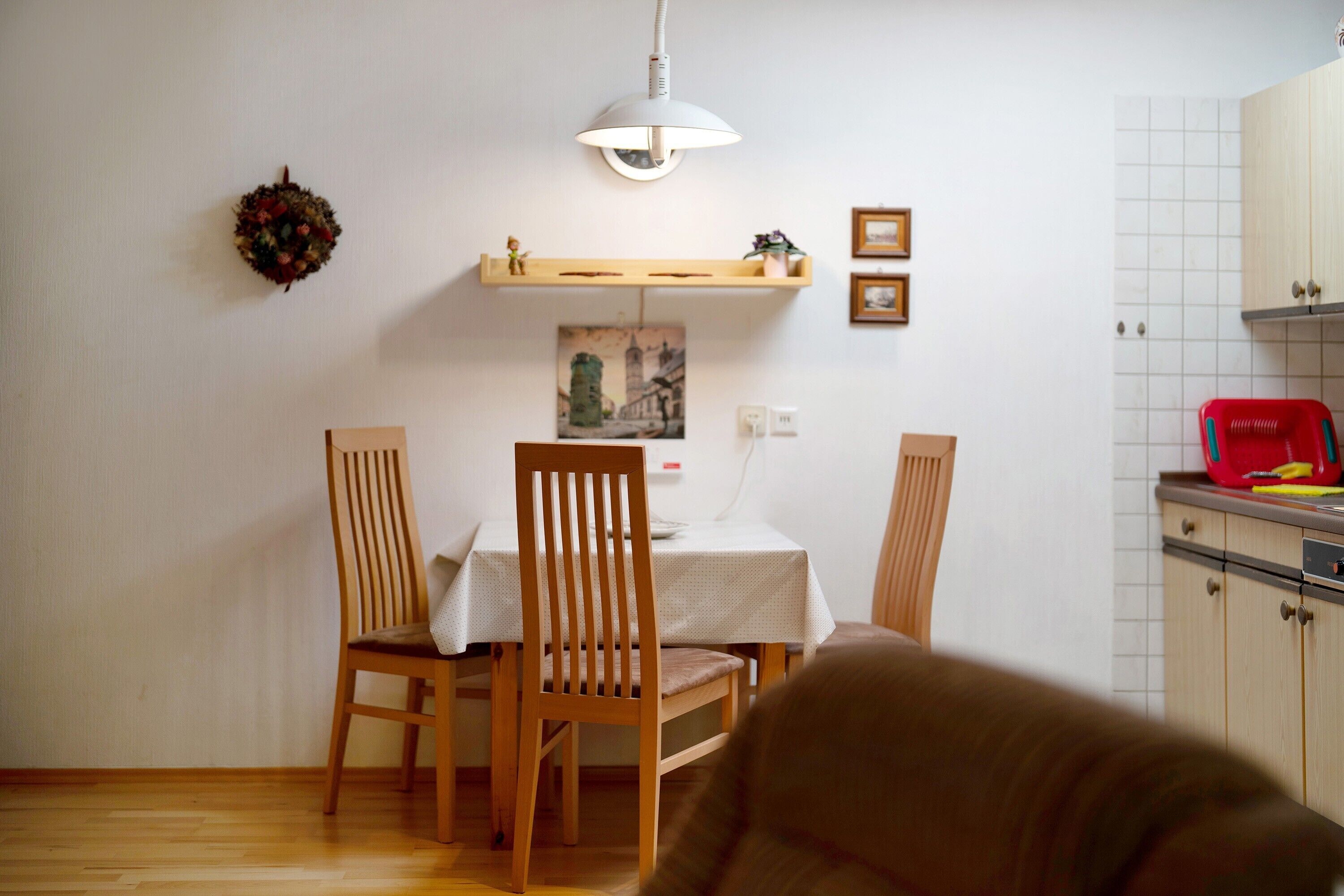 Ein Essbereich mit Tisch, Stühlen, einer Pendelleuchte, einem Regal mit Gegenständen und einem Wandbild.