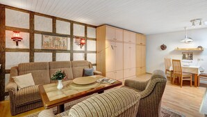 A living room with a sofa, armchair, wooden coffee table, and a dining area with chairs and a table. - Studio '3' with Private Terrace, Shared Garden and Wi-Fi (Schönwald im Schwarzwald)