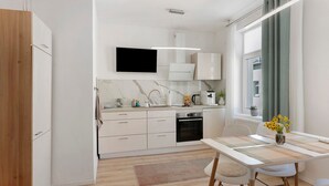 A modern kitchen with white cabinetry, a flat-screen TV, and a dining area with a table and chairs. - Apartment 'Baba' with Wi-Fi in Gera (Gera)