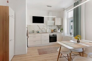 A modern kitchen with white cabinetry, a flat-screen TV, and a dining area with a table and chairs. - Apartment 'Baba' with Wi-Fi in Gera (Gera)