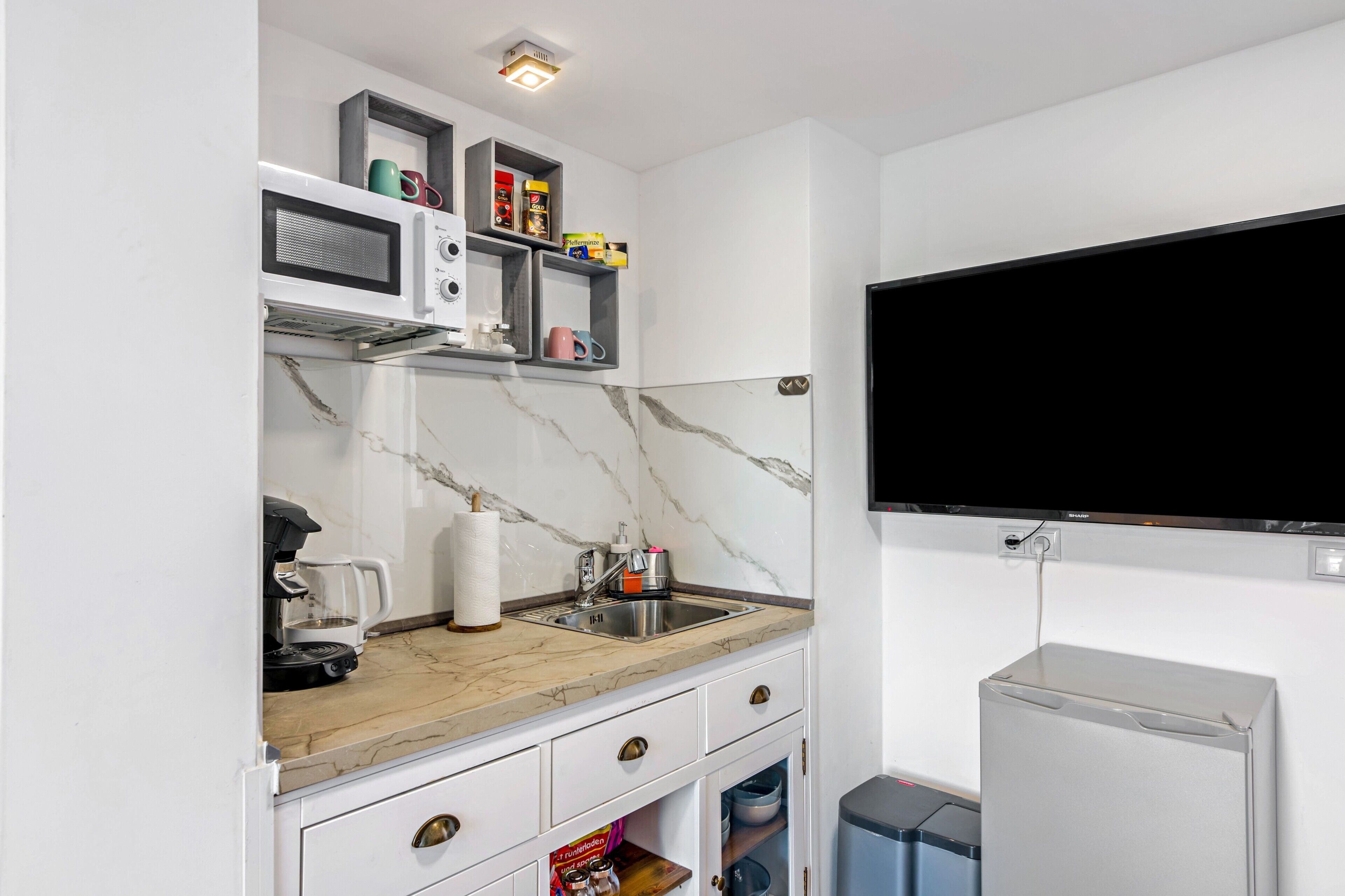 Eine kompakte Küche mit Mikrowelle, Kaffeemaschine und einem an der Wand befestigten Fernseher.