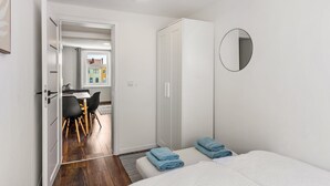 A bedroom with a bed, a wardrobe, a mirror, and a view into another room with a table and chairs.