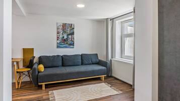Un salon moderne avec un canapé gris, une table basse en bois, un fauteuil jaune, un tapis blanc et un tableau représentant un paysage urbain accroché au mur.