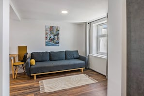 A modern living room with a grey sofa, a wooden coffee table, a yellow chair, a white rug, and a cityscape painting on the wall. - Apartment 'Desniq' with Wi-Fi in Gera (Gera)