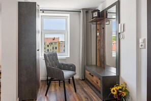 Una habitación con ventana, una silla, un espejo y una pequeña mesa con un florero.
