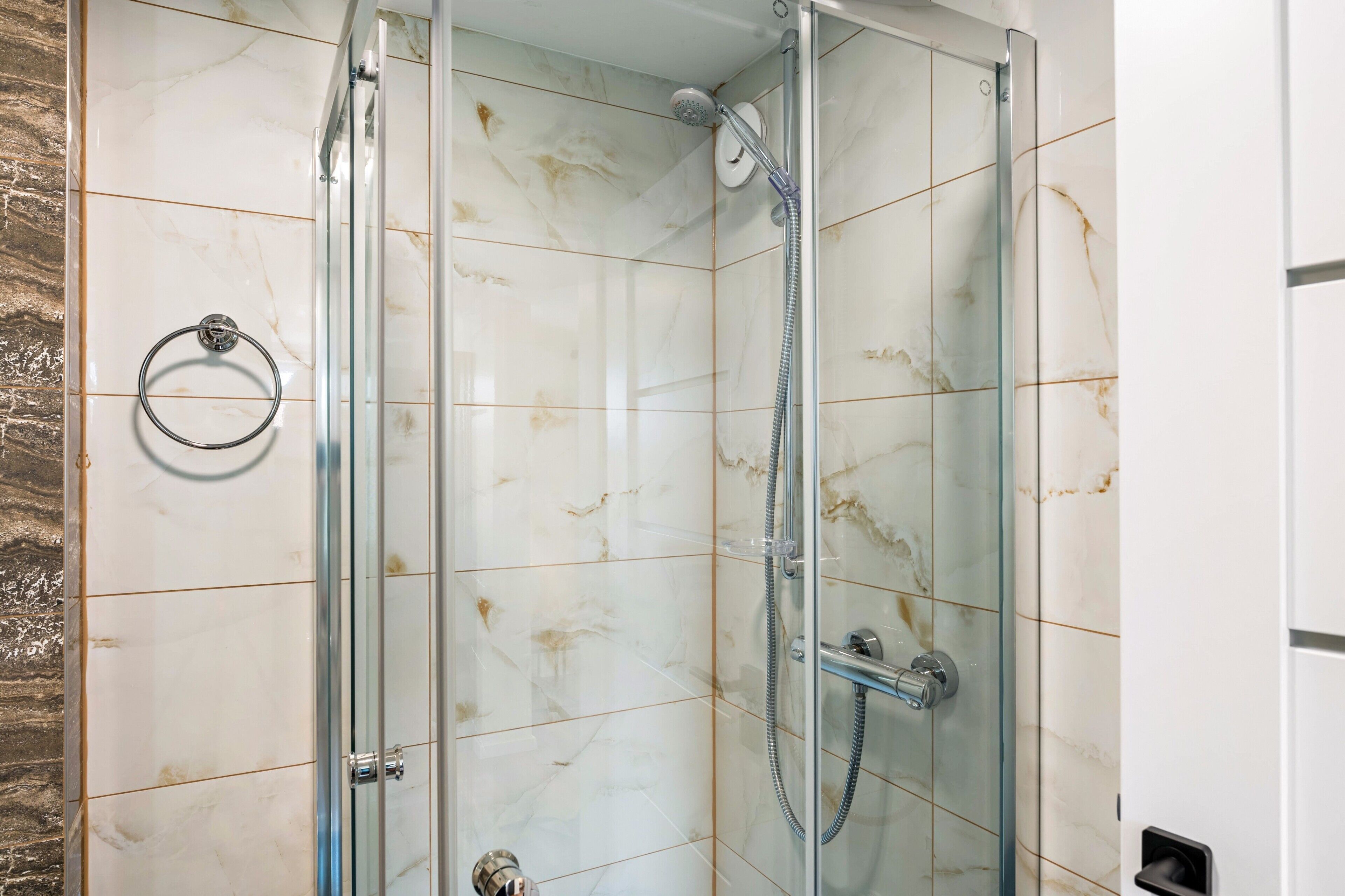 Eine Duschkabine mit Handbrause und am Wand montiertem Wasserhahn.