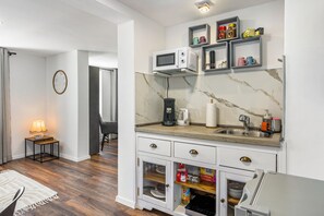Una cocina compacta con microondas, cafetera y armarios de almacenamiento.