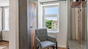A modern room with a large window, a grey upholstered chair, and a wooden wardrobe.