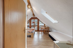 Ein Schlafzimmer im Loft-Stil mit schrägemausertem Dach, einem Holzbett, einem kleinen Tisch und Blick durch ein Fenster.
