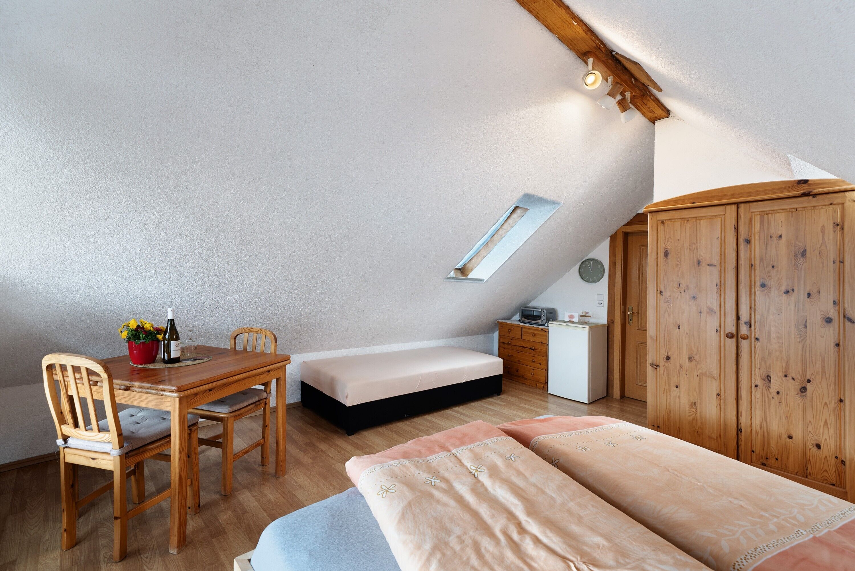 A bedroom with a loft bed, a wooden desk, a chair, a small bedside table, and a wardrobe.