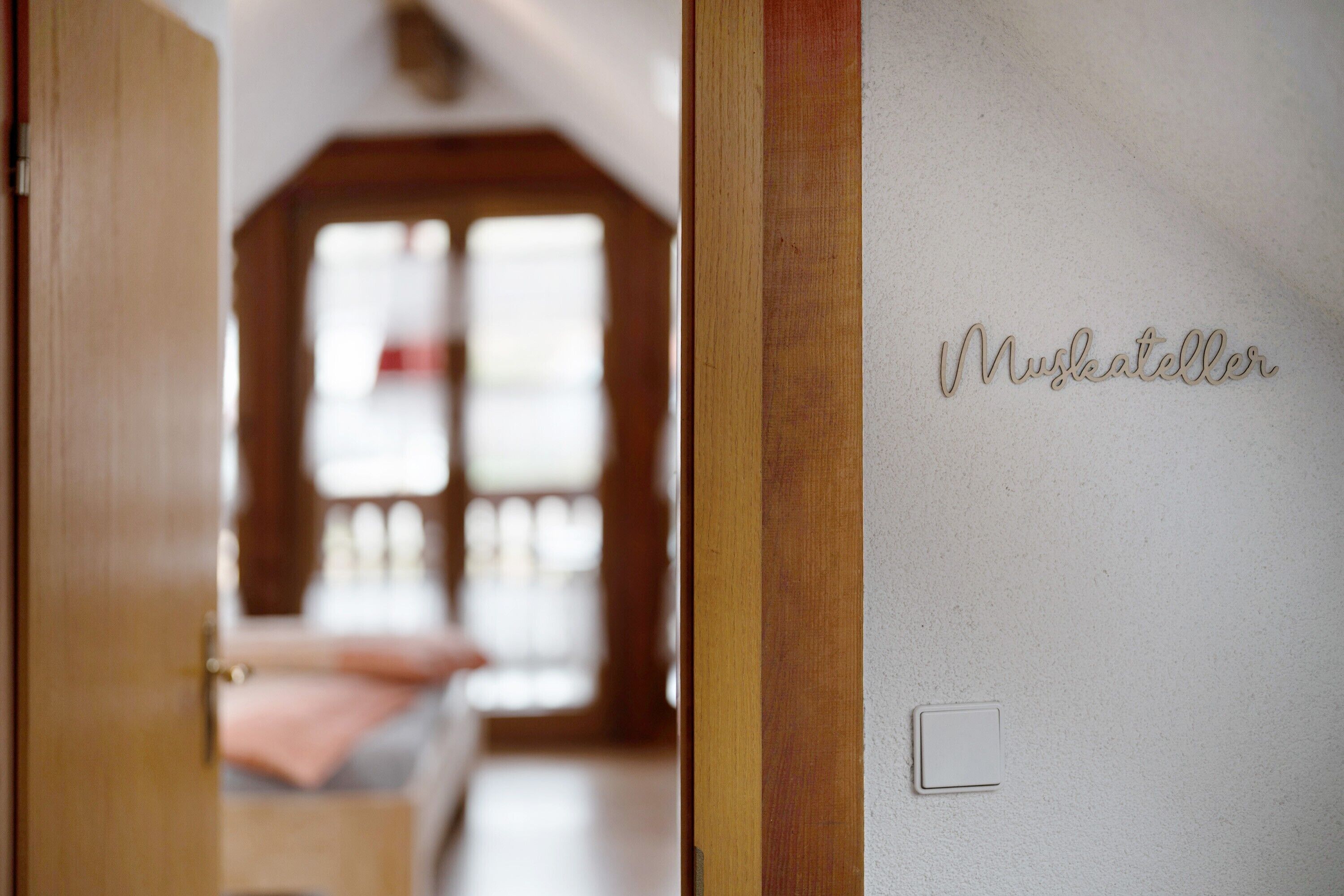 Una habitación de hotel con una puerta de madera, una cama con una manta rosa y una pared con el nombre 'Muskateller'.