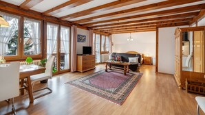 A spacious room with wooden beams, a dining area, a sofa, and a large window.
