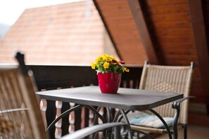 A table with a red pot of yellow flowers, a wicker chair, and a wooden ceiling.
